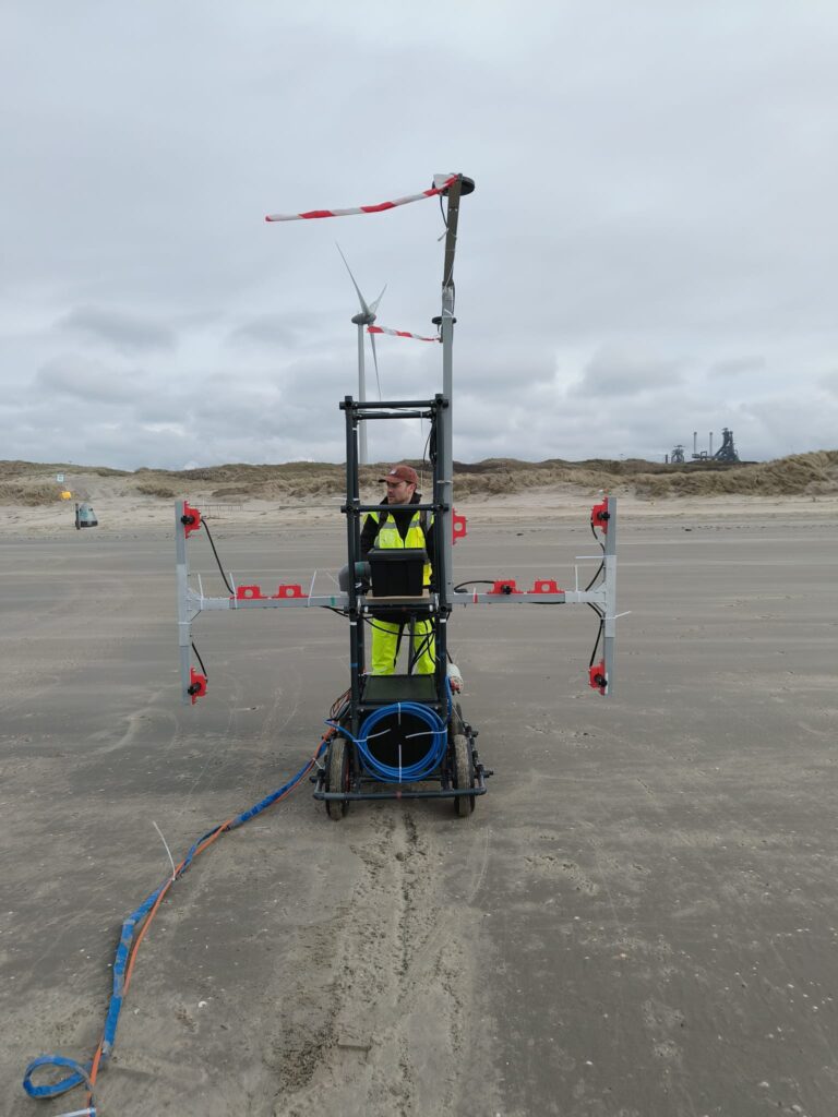 Engineer operating onshore survey cart with mounted sensors on a beach, conducting buried cable detection near wind farm.